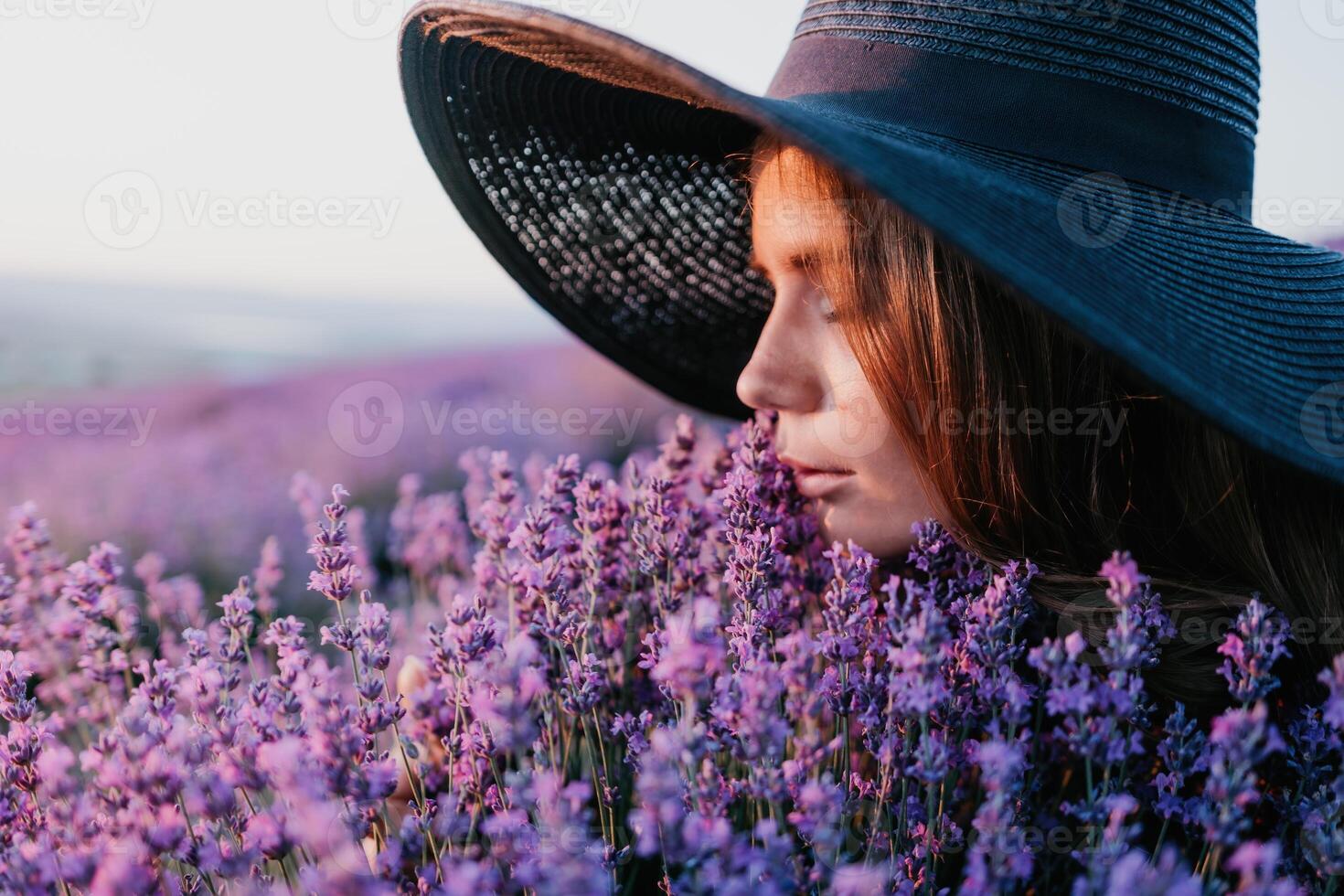 Woman lavender field. Happy carefree woman in black dress and hat with large brim smelling a blooming lavender on sunset. Perfect for inspirational and warm concepts in travel and wanderlust. Close up photo