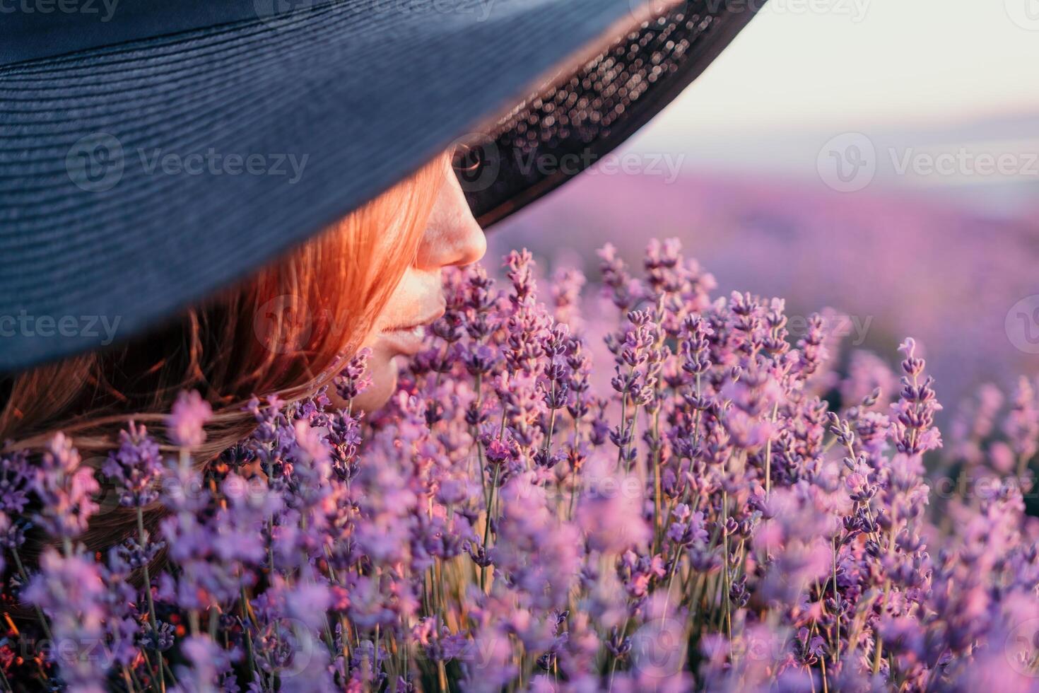 Woman lavender field. Happy carefree woman in black dress and hat with large brim smelling a blooming lavender on sunset. Perfect for inspirational and warm concepts in travel and wanderlust. Close up photo