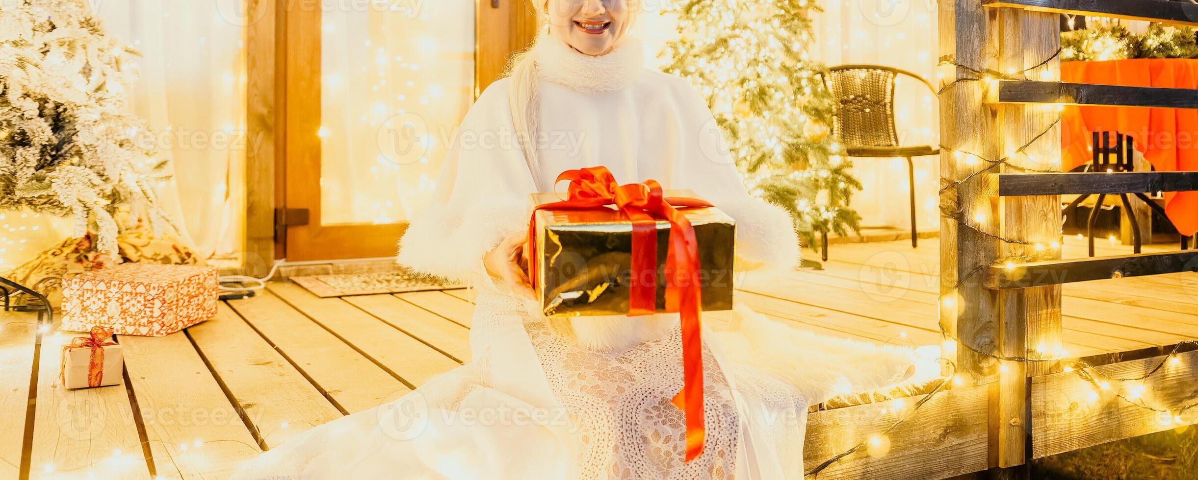 contento sonriente mujer en un blanco vestir participación un regalo caja en frente de un Navidad árbol. foto