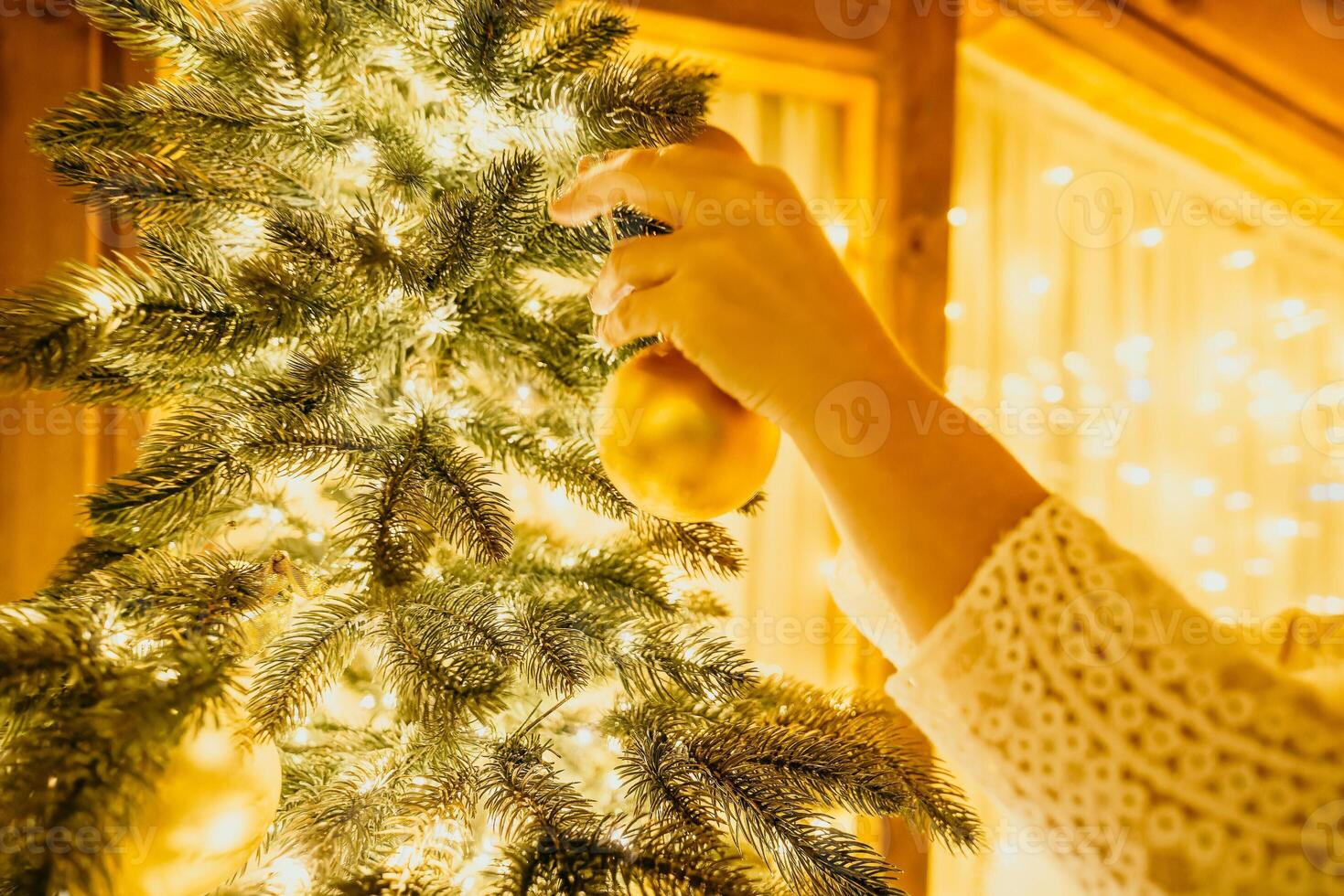 Woman decorate A Christmas tree with gold ornaments and lights. The tree is decorated with gold balls and is lit up with lights. photo