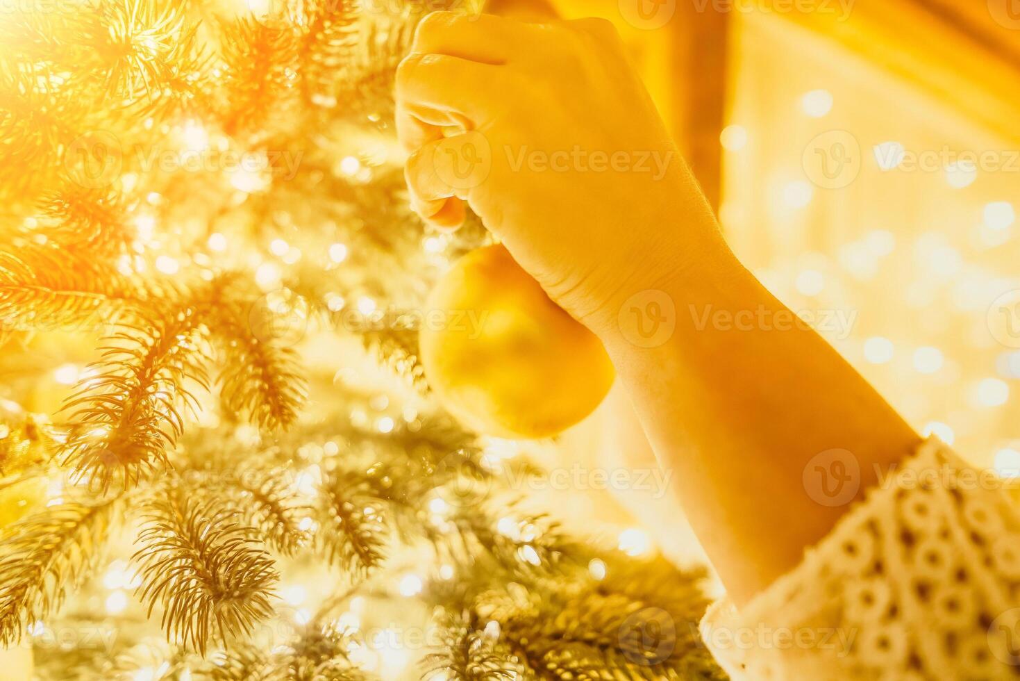 Woman decorate A Christmas tree with gold ornaments and lights. The tree is decorated with gold balls and is lit up with lights. photo
