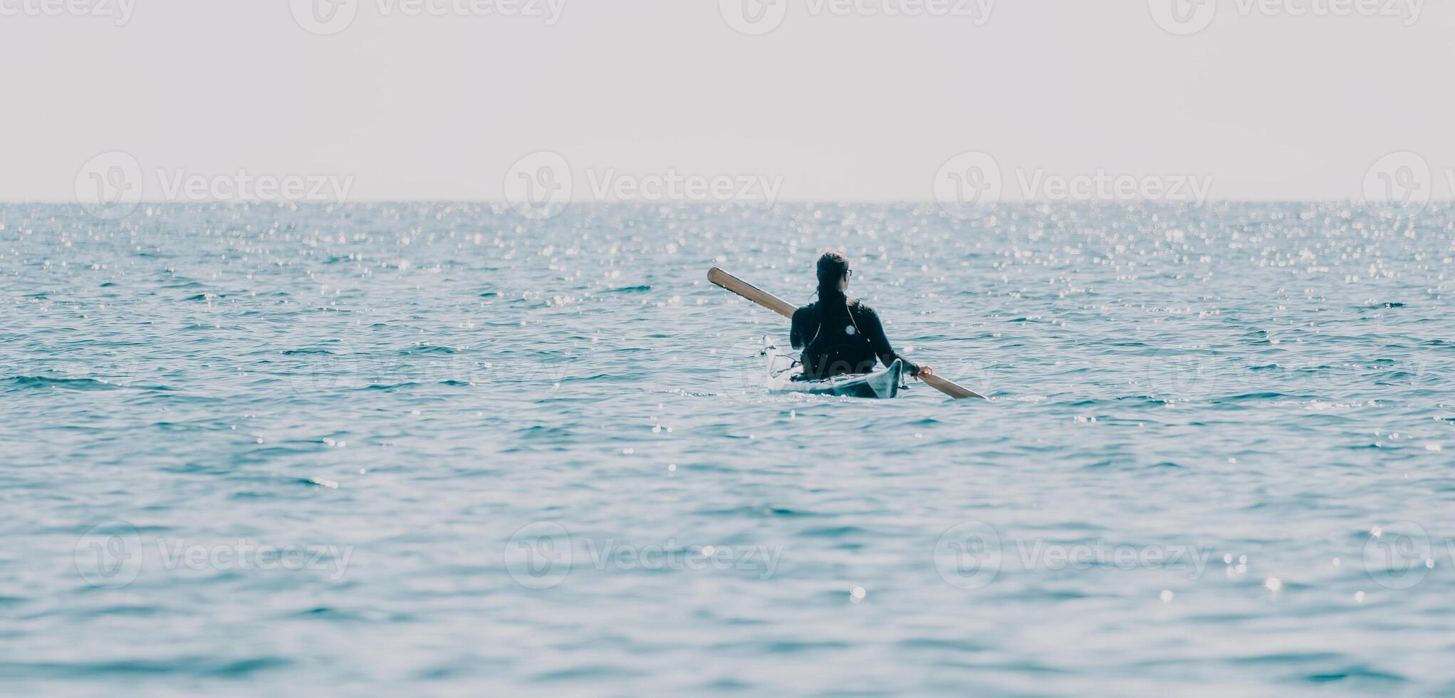 Woman sea kayak. Happy smiling woman in kayak on ocean, paddling with wooden oar. Calm sea water and horizon in background. Active lifestyle at sea. Summer vacation. photo