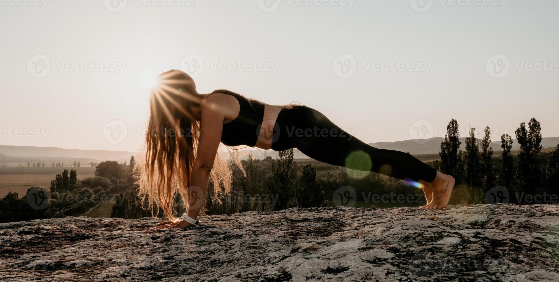 Fitness woman. Well looking middle aged woman with long hair, fitness instructor in leggings and tops doing stretching and pilates on the rock near forest. Female fitness yoga routine concept. photo