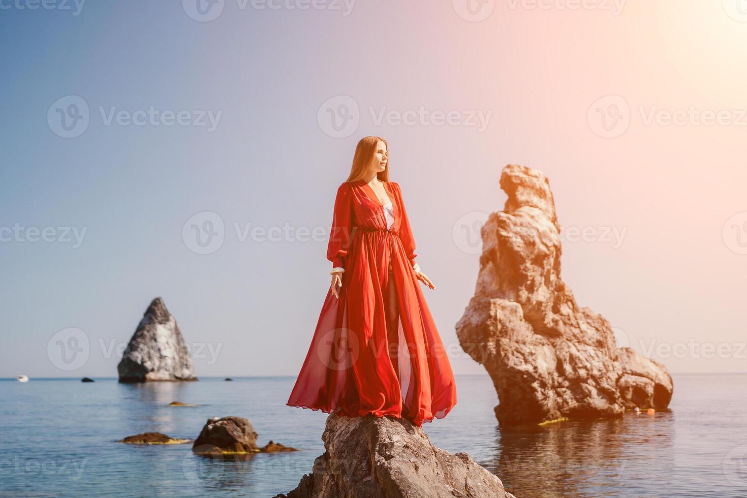 Woman travel sea. Young Happy woman in a long red dress posing on a beach near the sea on background of volcanic rocks, like in Iceland, sharing travel adventure journey photo