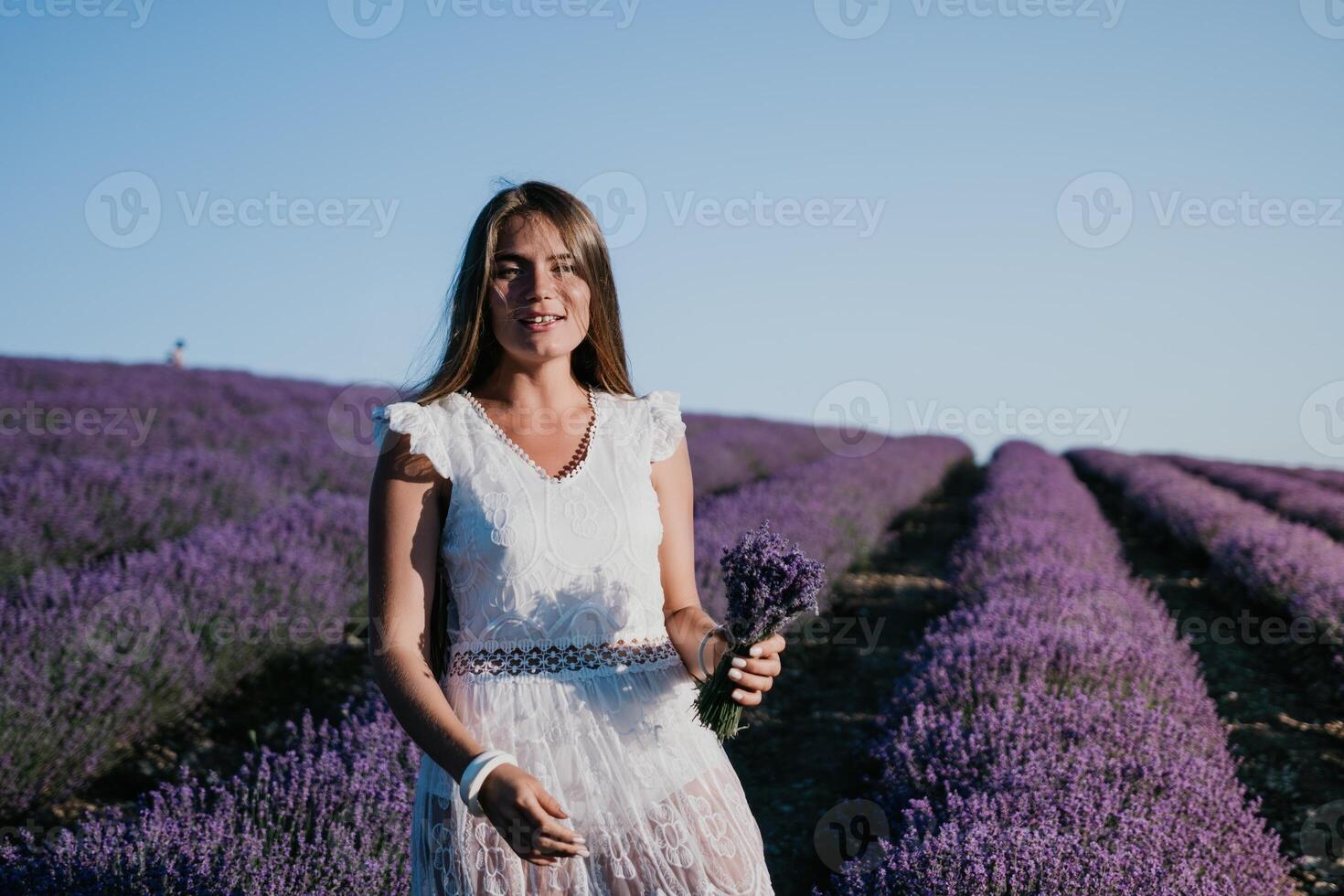 Woman lavender field. Happy carefree woman in a white dress walking in a lavender field and smelling a lavender bouquet on sunset. Ideal for warm and inspirational concepts in wanderlust and travel. photo