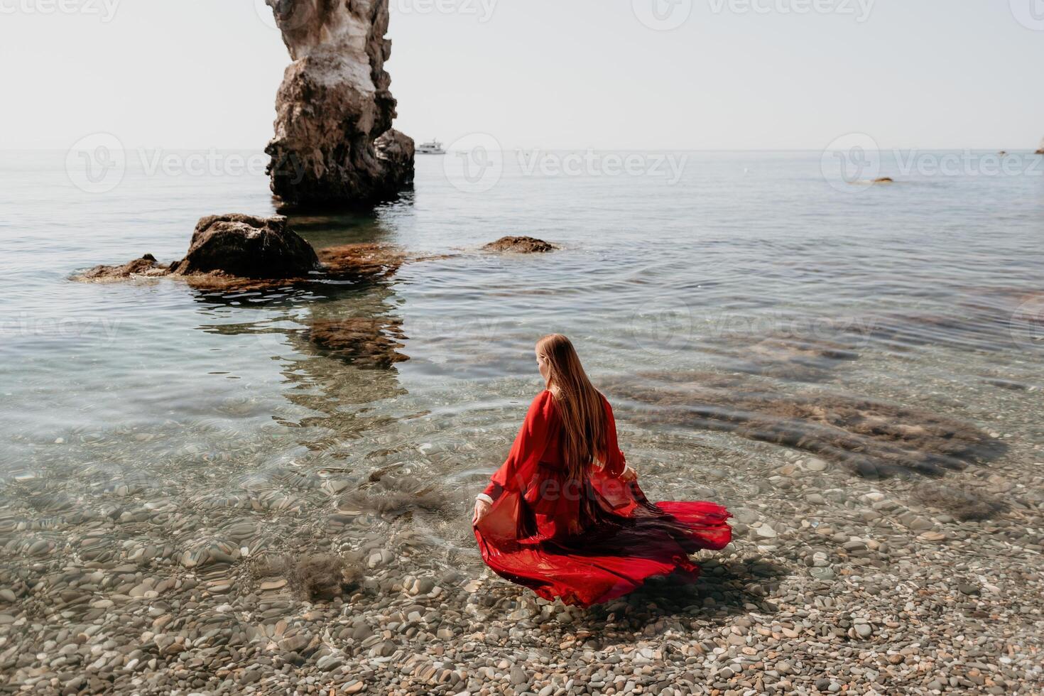 Woman travel sea. Happy tourist in red dress enjoy taking picture outdoors for memories. Woman traveler posing on the rock at sea bay surrounded by volcanic mountains, sharing travel adventure journey photo