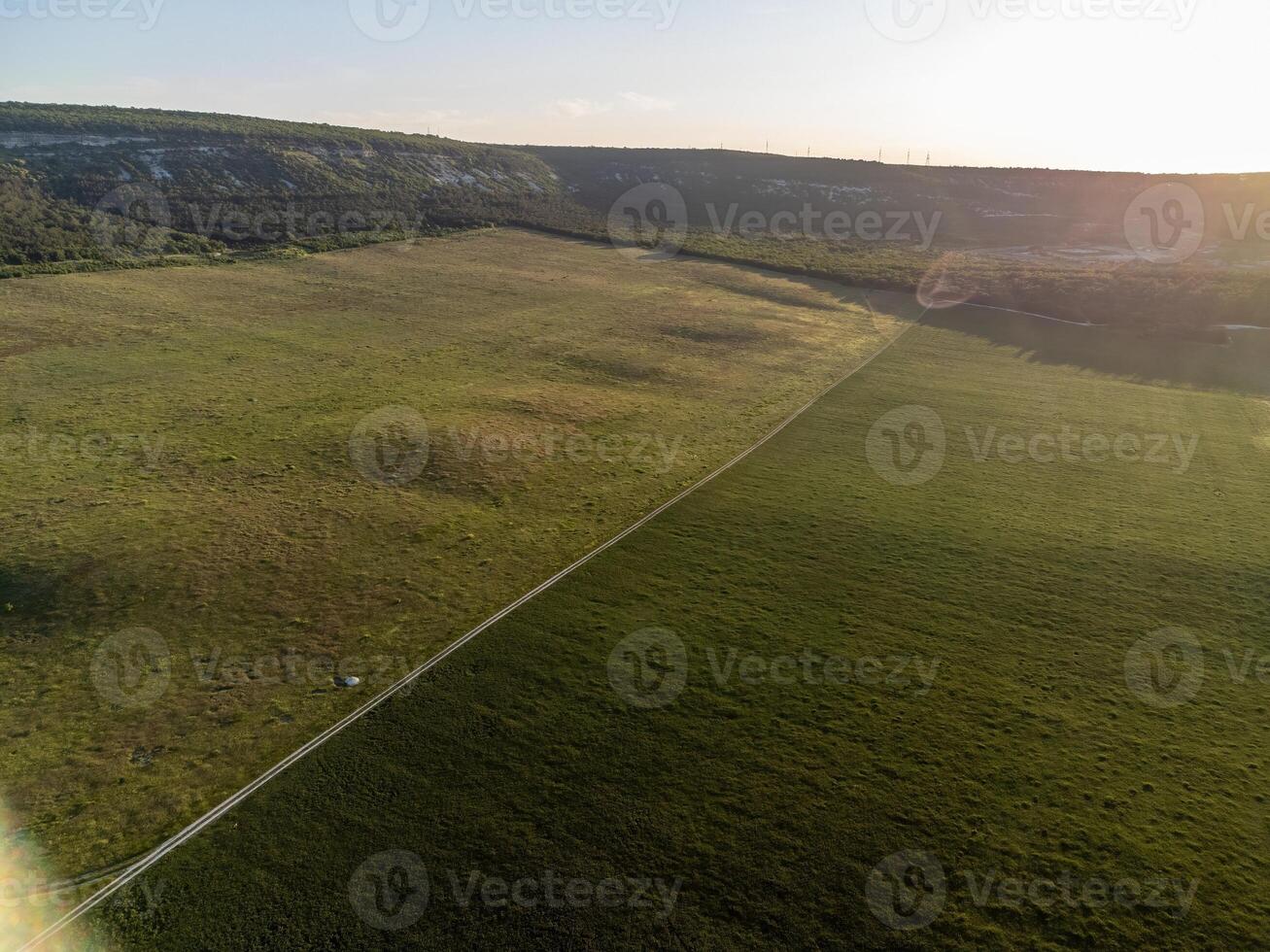 Aerial view on green wheat field, road and hills in countryside. Field of wheat blowing in the wind on sunset. Ears of barley crop in nature. Agronomy, industry and food production. photo
