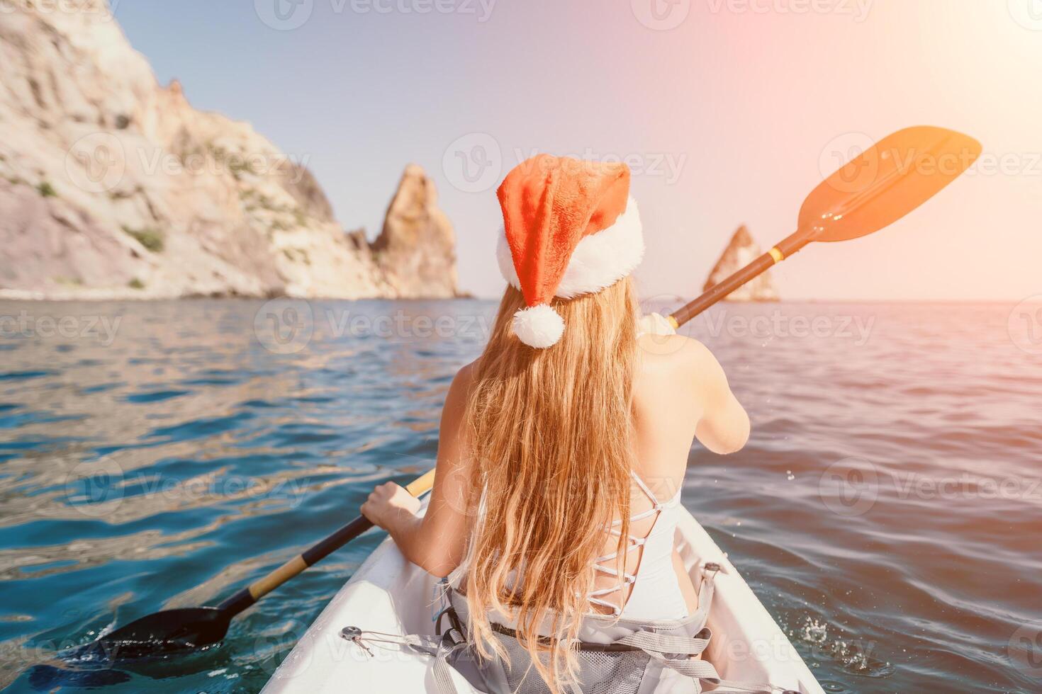 Woman in kayak back view. Happy young woman in Santa hat floating in kayak on calm sea. Summer holiday vacation and cheerful female people relaxing having fun on the boat. photo