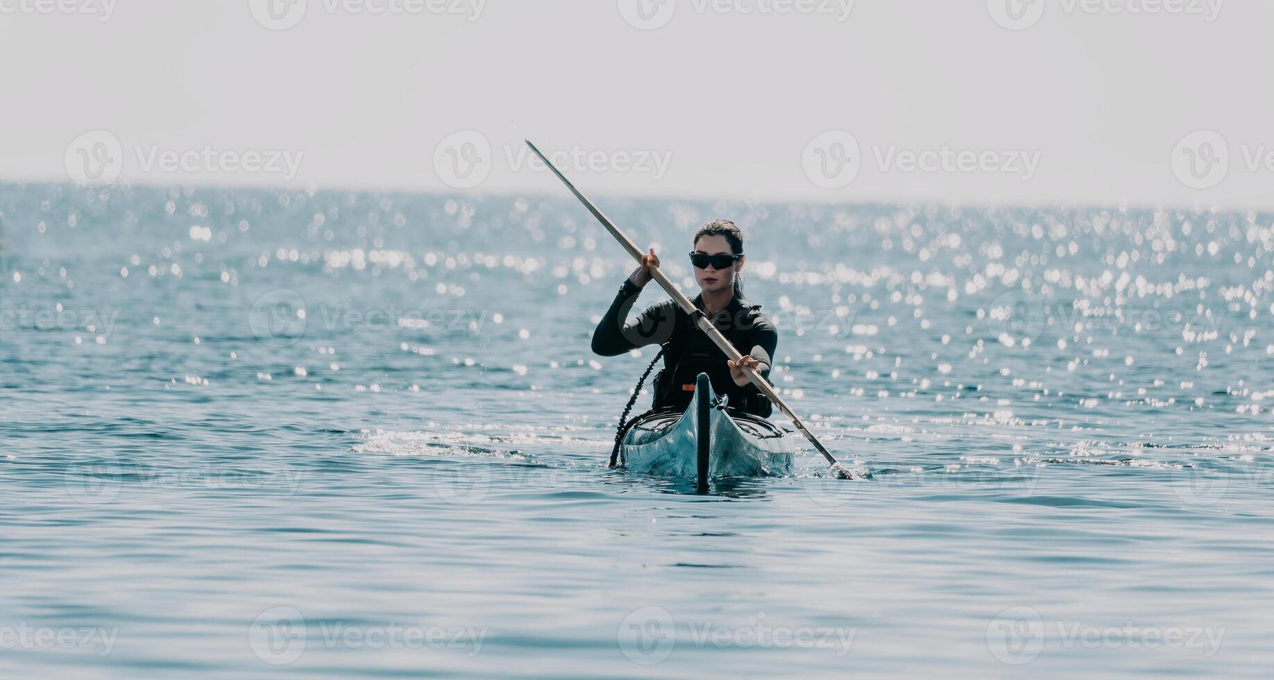 Woman sea kayak. Happy smiling woman in kayak on ocean, paddling with wooden oar. Calm sea water and horizon in background. Active lifestyle at sea. Summer vacation. photo