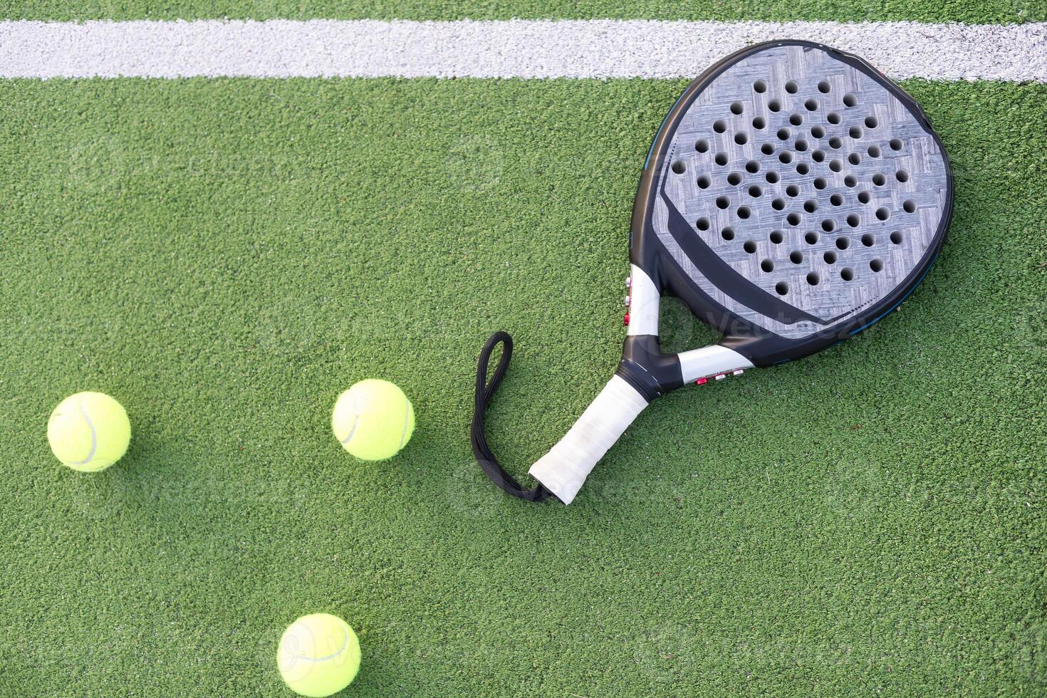 Blue padel racket and yellow balls placed on court near net on sunny day photo