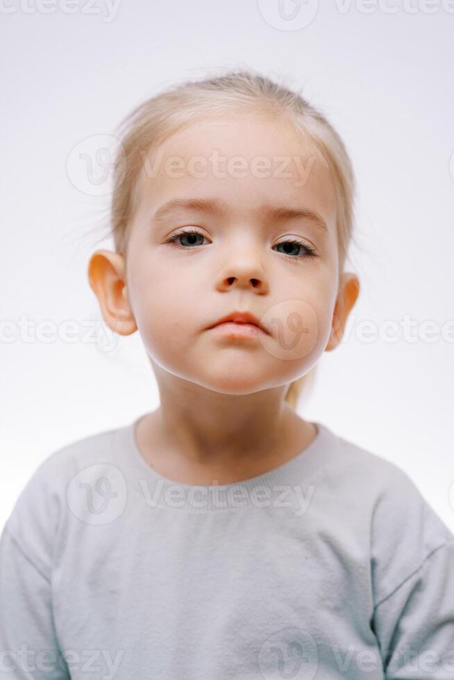 Portrait of a little serious sad girl on a gray background photo