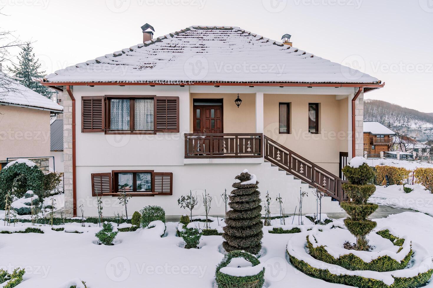 artísticamente recortado verde arbustos en el cubierto de nieve yarda de un dos pisos casa foto