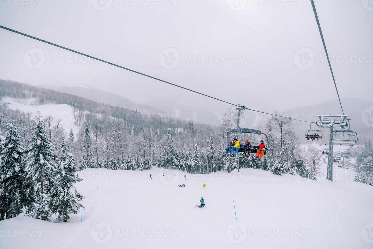 Tourists ride on a chairlift above the forest and ski slope with skiers skiing photo