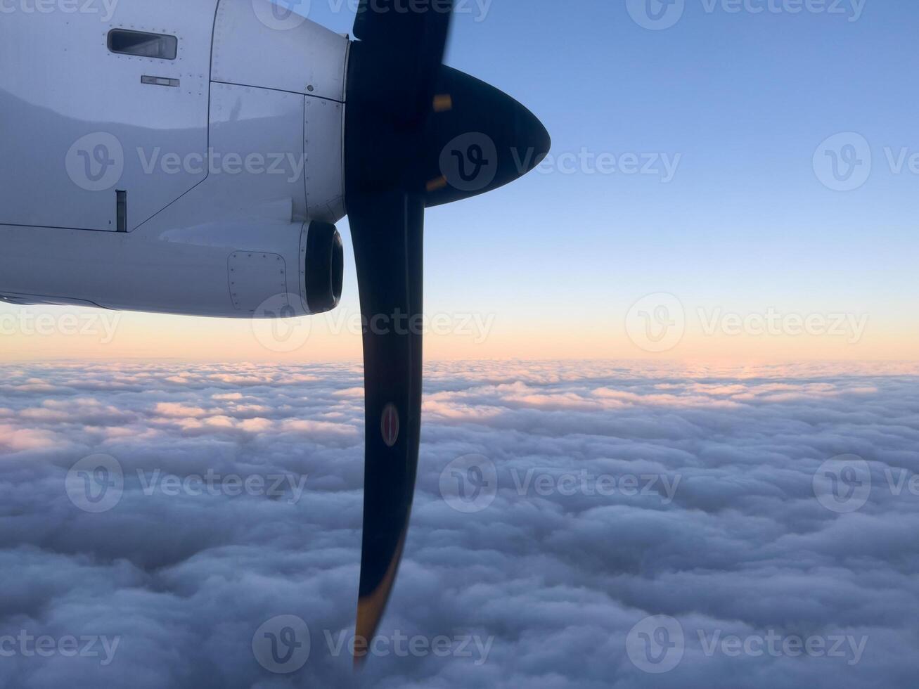 Rotating propeller of an airplane flying above the clouds in the sunset sky photo