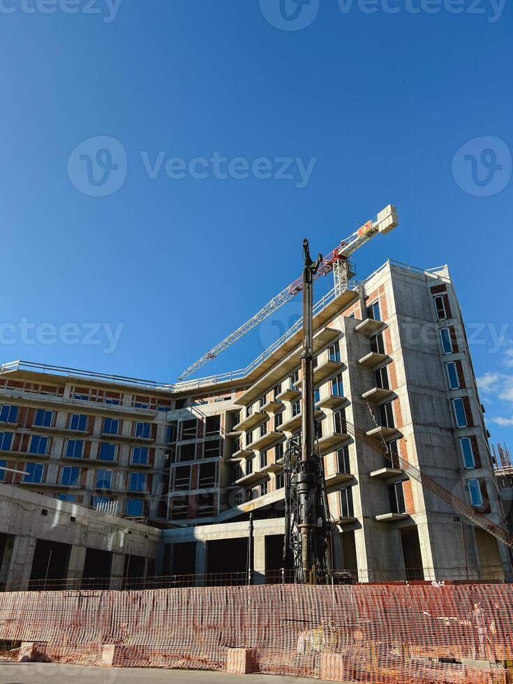 Construction crane stands behind a fence near a multi-storey building photo