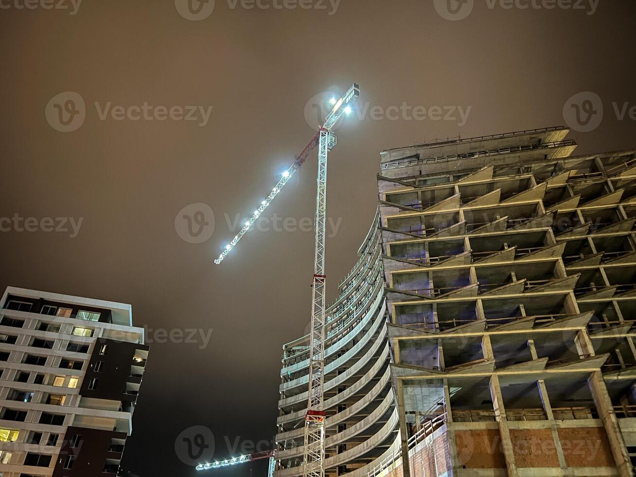 Illuminated tower crane builds a large multi-storey building against a dark sky photo