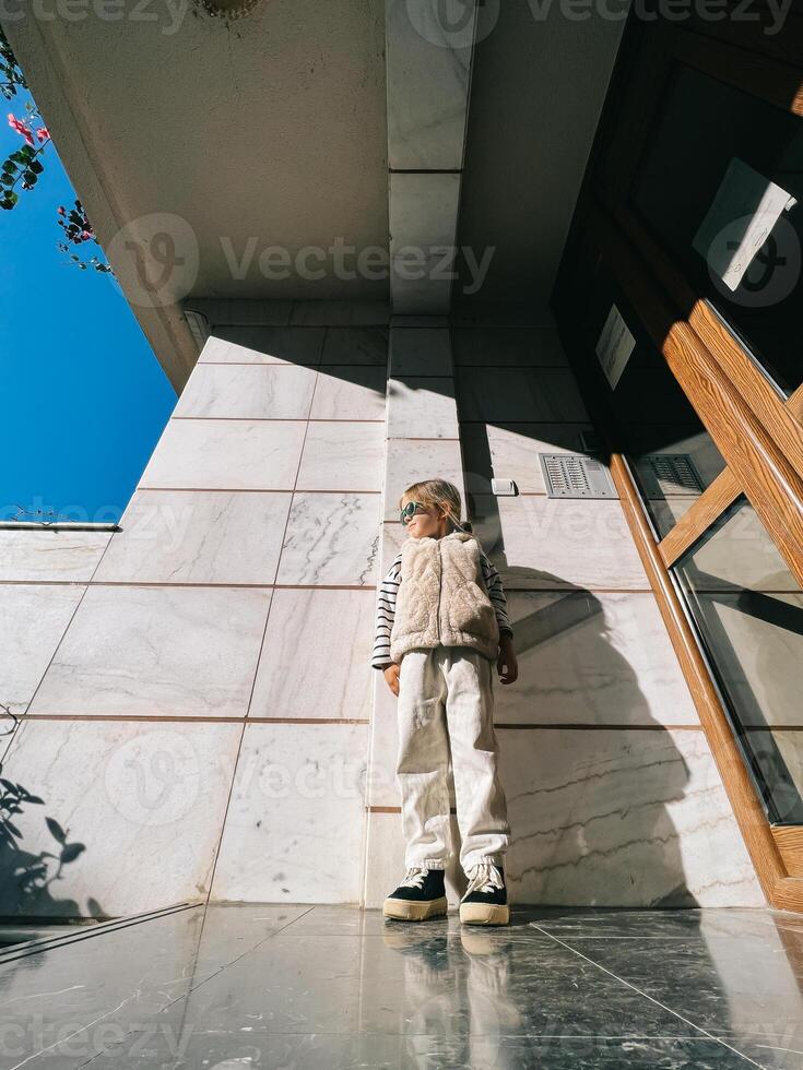 Little girl in sunglasses posing against the background of the wall at home photo
