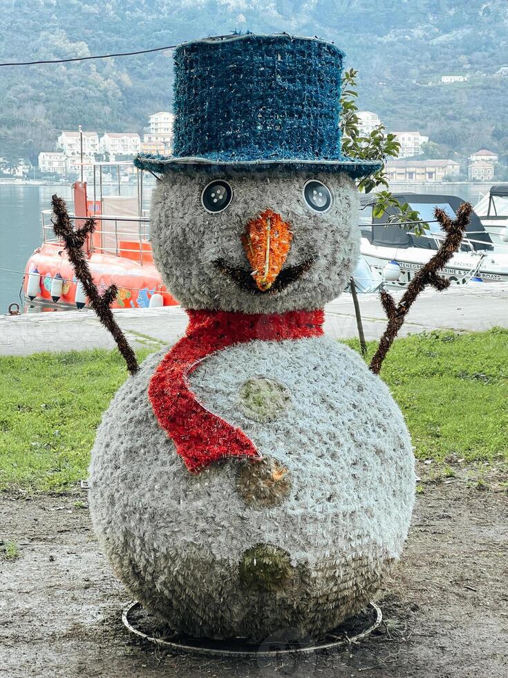 Sculpture of a snowman in a hat with a scarf stands on the seashore photo