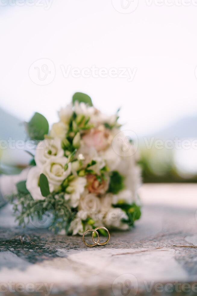 Pair of wedding rings stands near the bride's lying bouquet photo