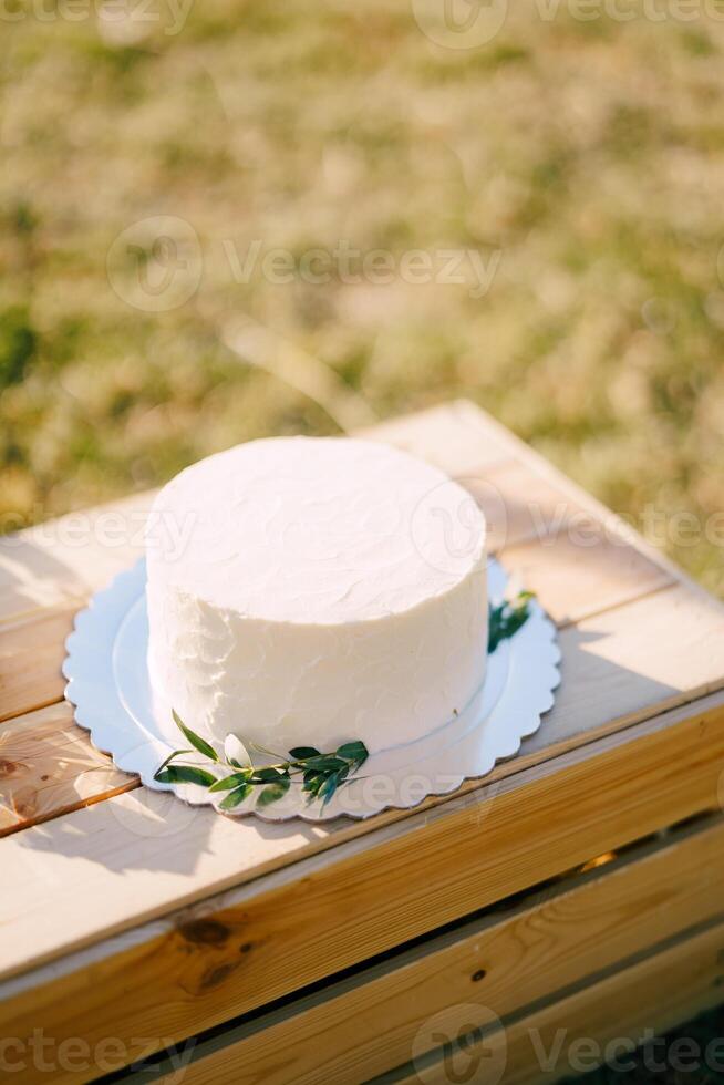 White wedding cake on a plate stands on a wooden box on a green lawn photo