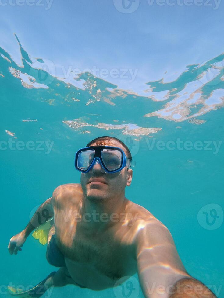 Young man in a swimming mask and fins swims underwater photo