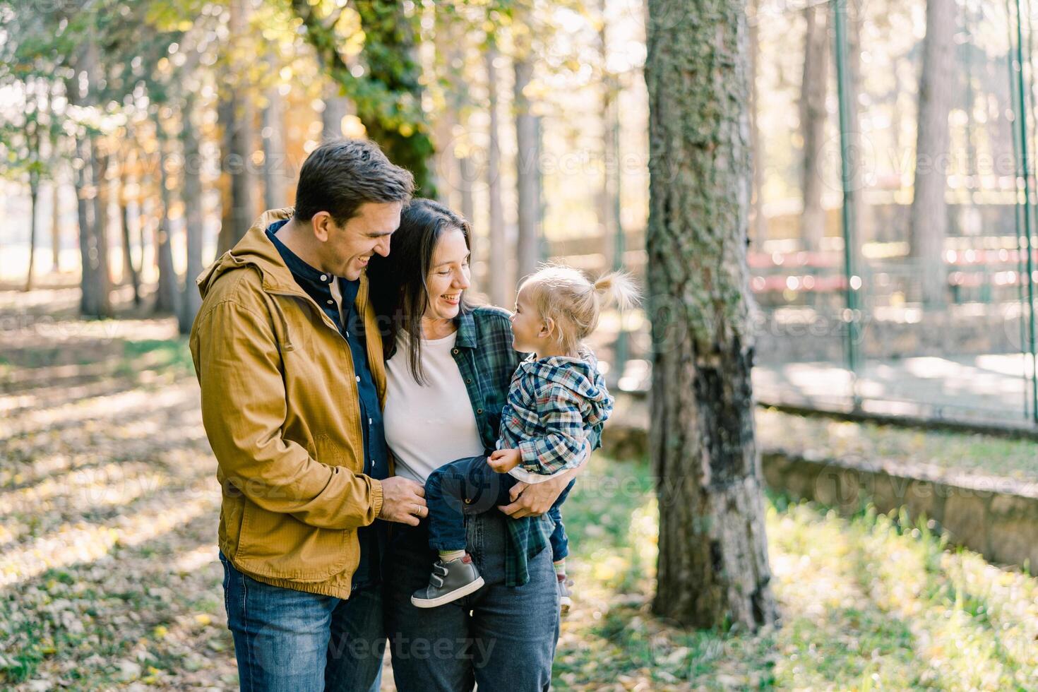 Dad hugs mom with a little girl in her arms while standing in the park photo