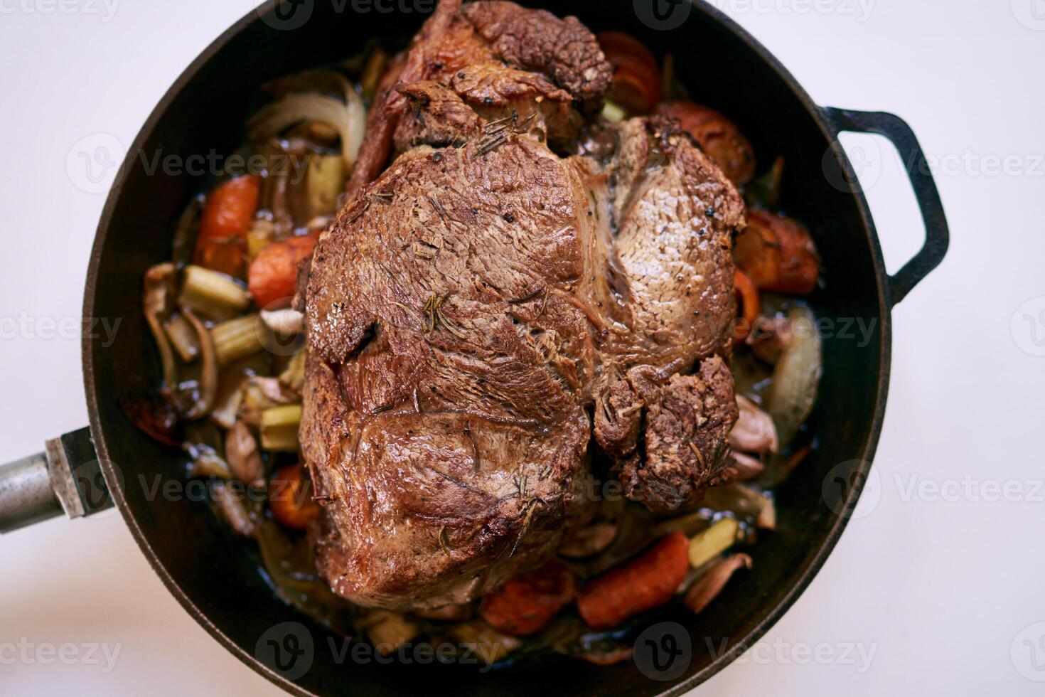 Frying pan with ruddy roast beef with vegetables stands on a white table. Top view photo