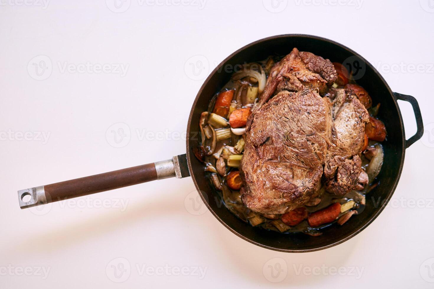 Frying pan with a wooden handle with roast beef and vegetables on a white table. Top view photo