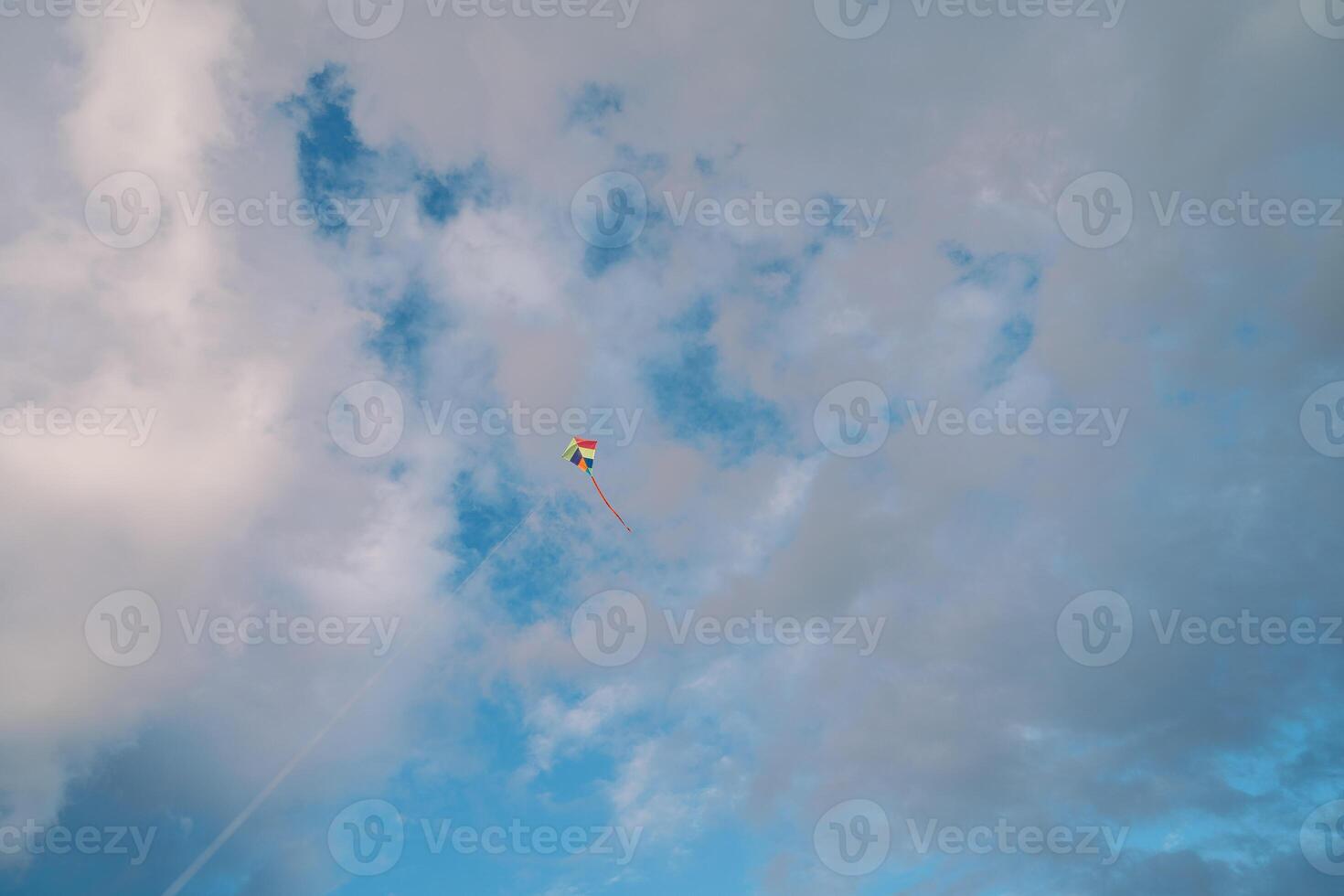 Colorful kite on a string soars in the cloudy sky photo