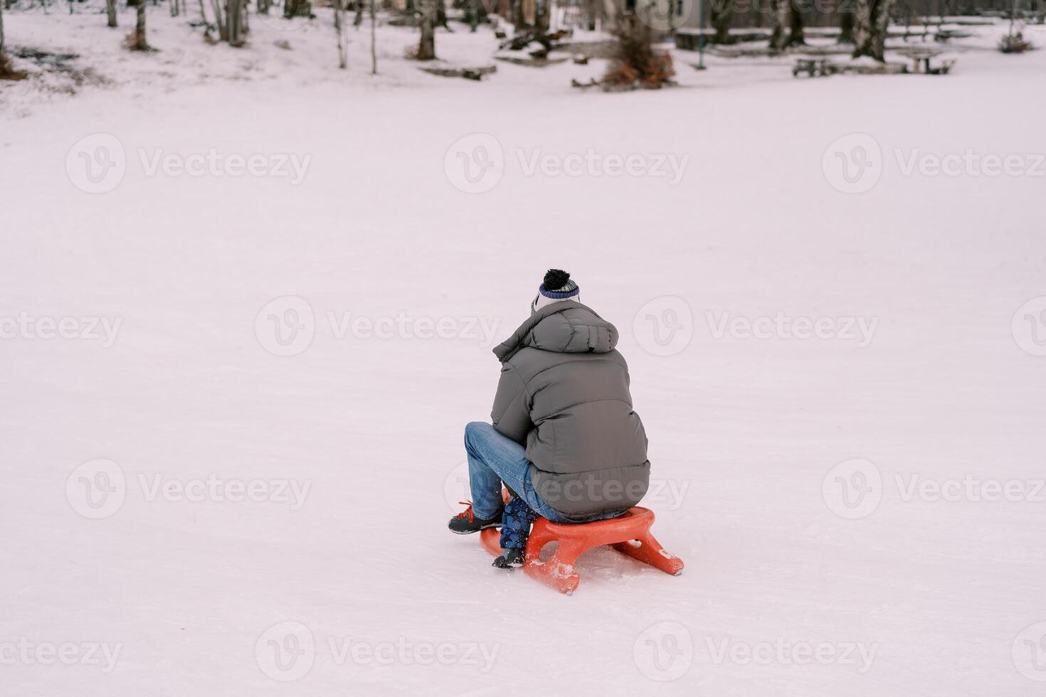 Dad and a small child are sledding on a snowy hill. Back view photo