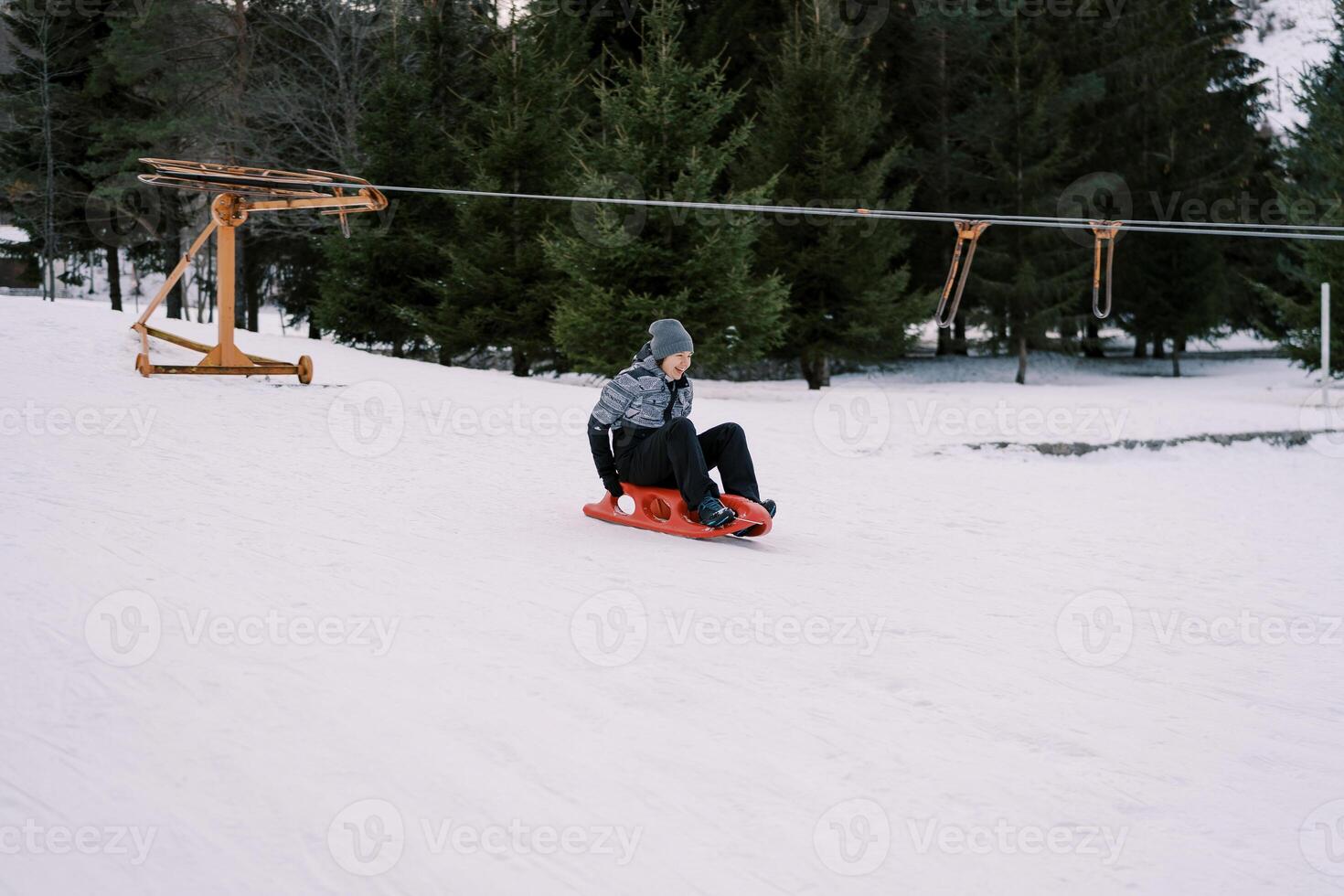 Laughing young woman rushes on a sled down a snowy slope past a rope lift photo