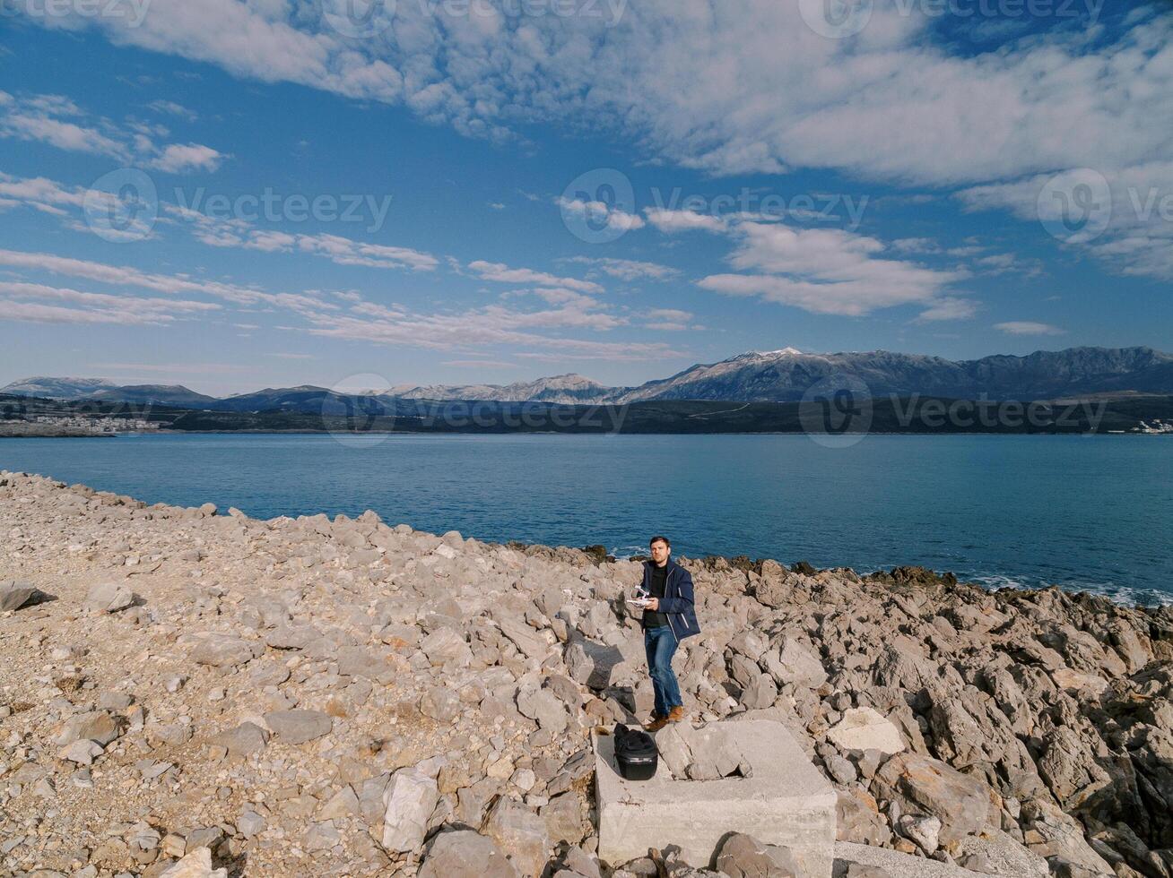 Operator with a drone remote control in his hands stands on a stone platform on a rocky seashore photo