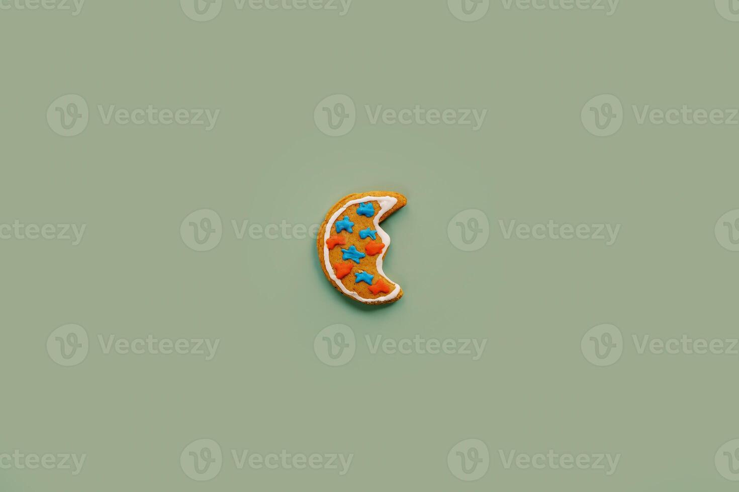 Cookie in the shape of a half moon with glazed stars lies on a green background photo
