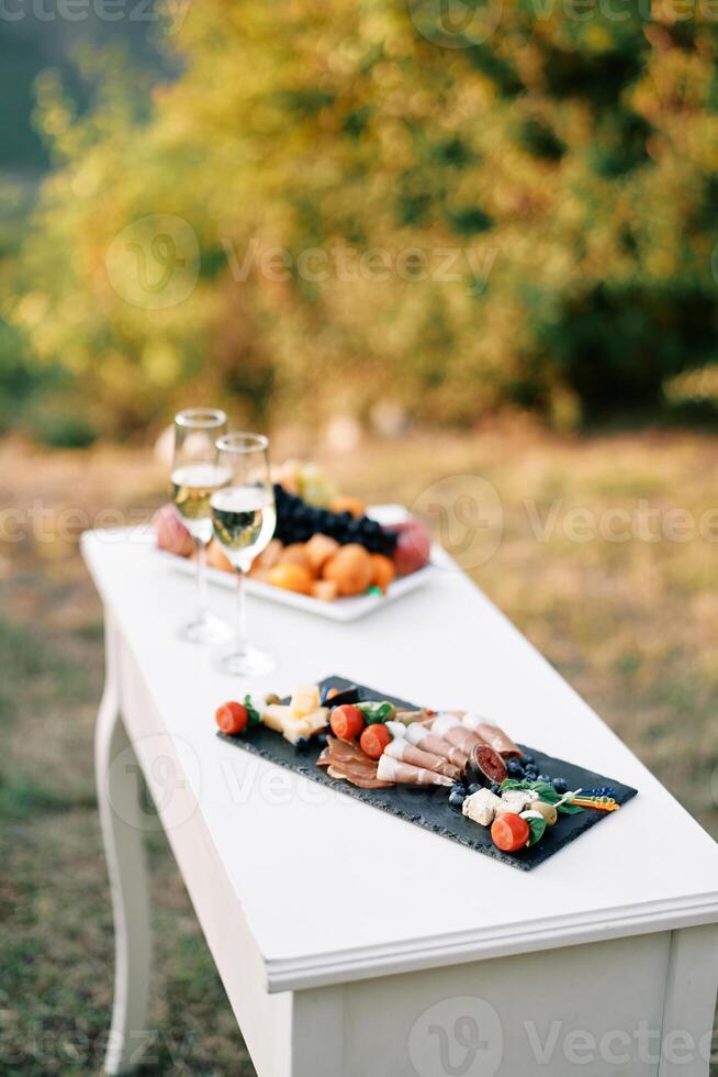 Small festive table with two glasses of champagne and snacks stands on the lawn photo