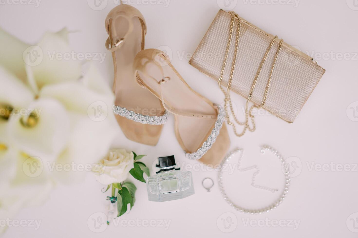 Wedding ring lies on a white table near the bride shoes, handbag and perfume. Top view photo