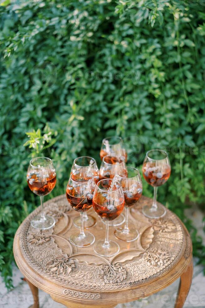 Glasses with red wine and floating grapes inside stand on a carved wooden table in the garden photo