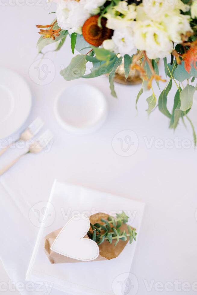 Invitation succulent in a pot with a paper heart on a set table with a bouquet of flowers photo