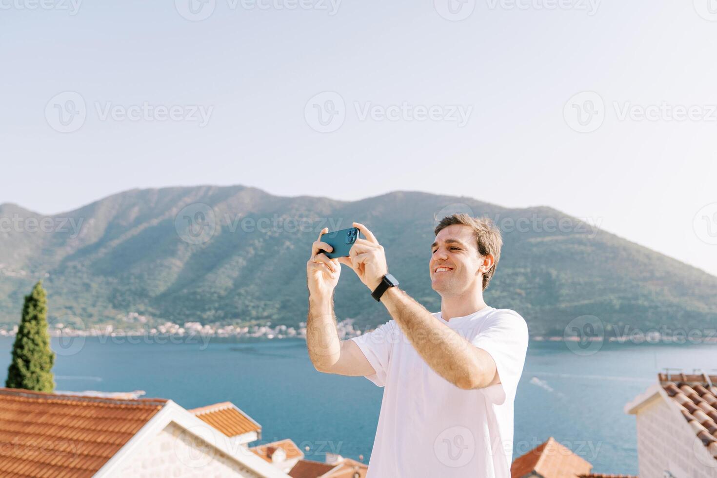 Smiling guy takes pictures of landscapes with a smartphone on an observation deck over the sea photo