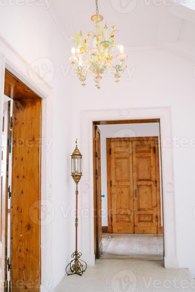 Colorful chandelier with floral decorations and pendants hangs on the ceiling near a wooden door in a room photo