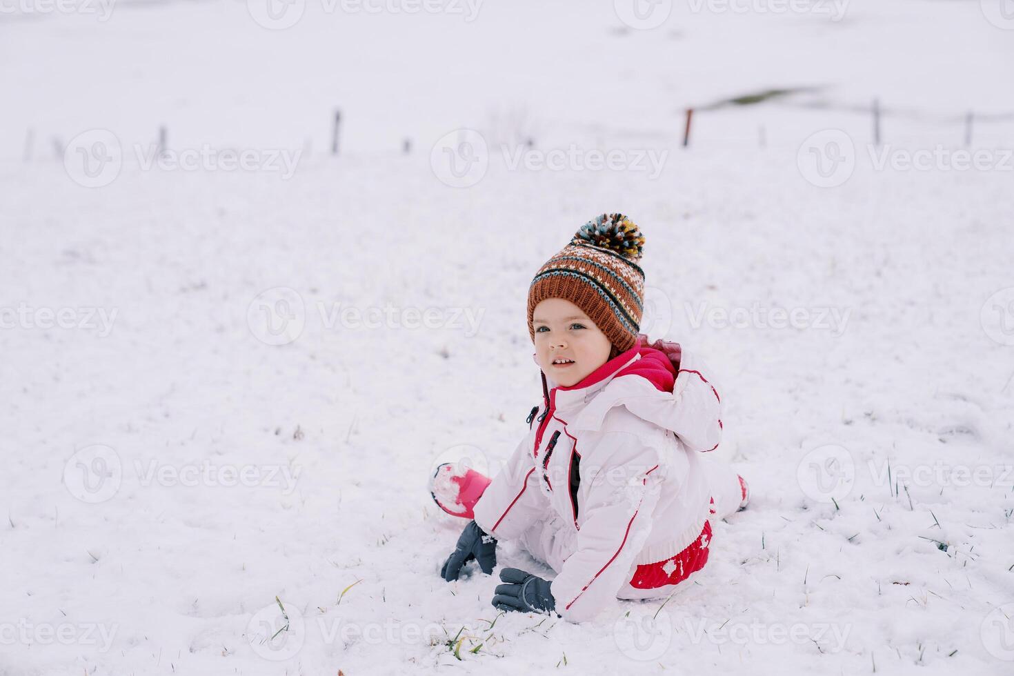 Little smiling girl sits half-turned on the snow photo