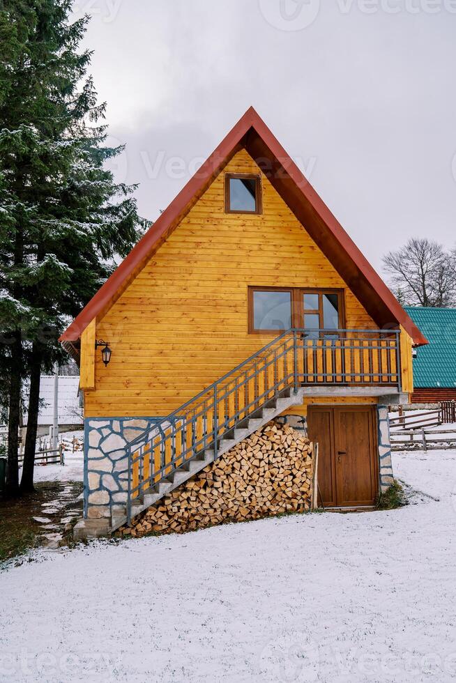 Two-story wooden cottage with a woodpile under the steps in a snowy forest photo