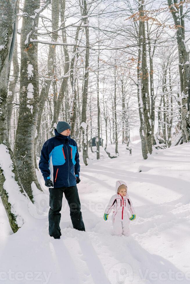 Dad and little girl stand in a snowy forest photo