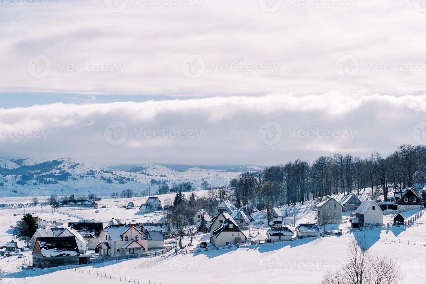 Nevado pueblo en un Pendiente rodeado por bosque foto