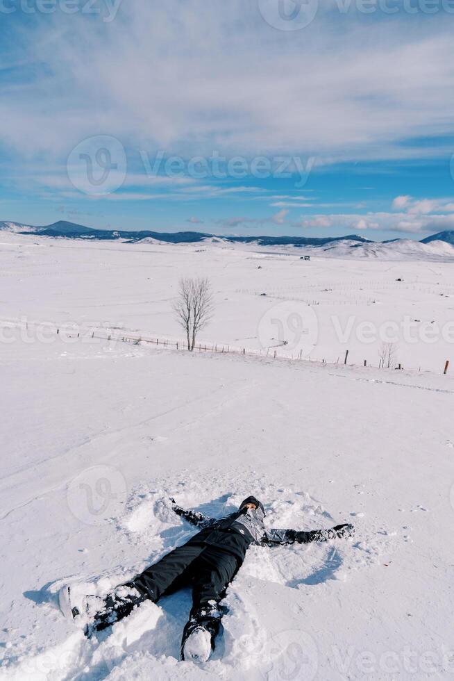 Girl in a ski suit makes a snow angel in the snow photo