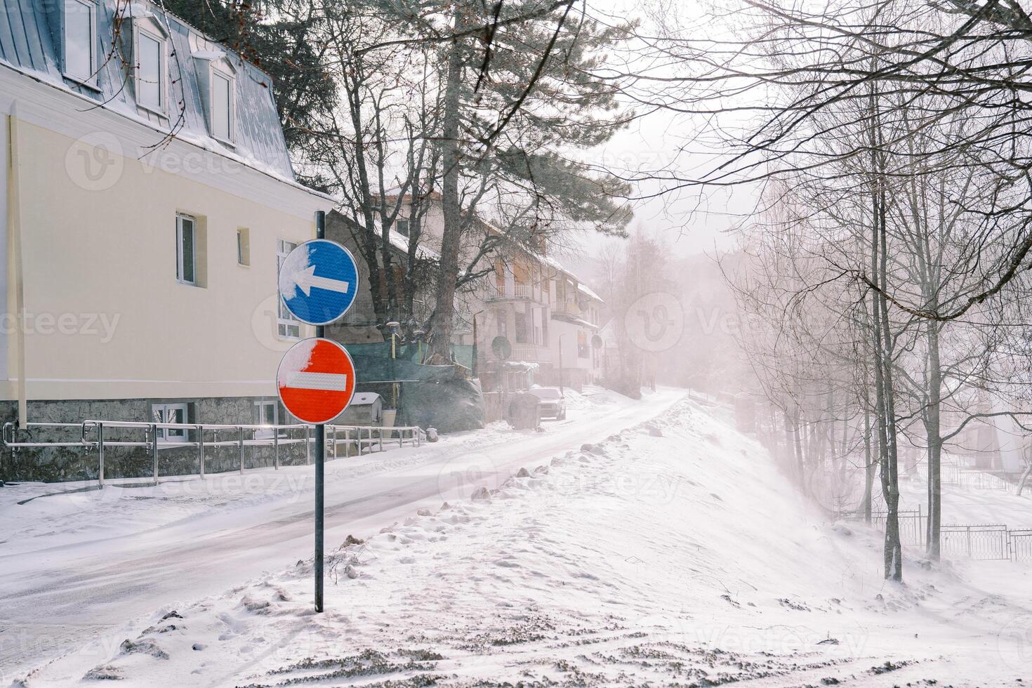 Stop and detour road signs stand on a snowy street near a building photo
