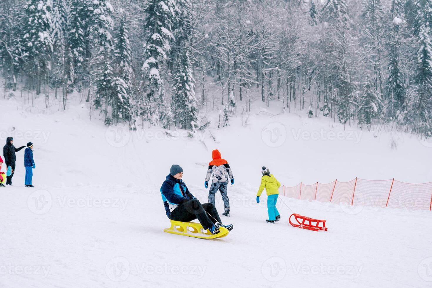 Young man rides a sled on a snow-covered mountain past climbing sledders photo