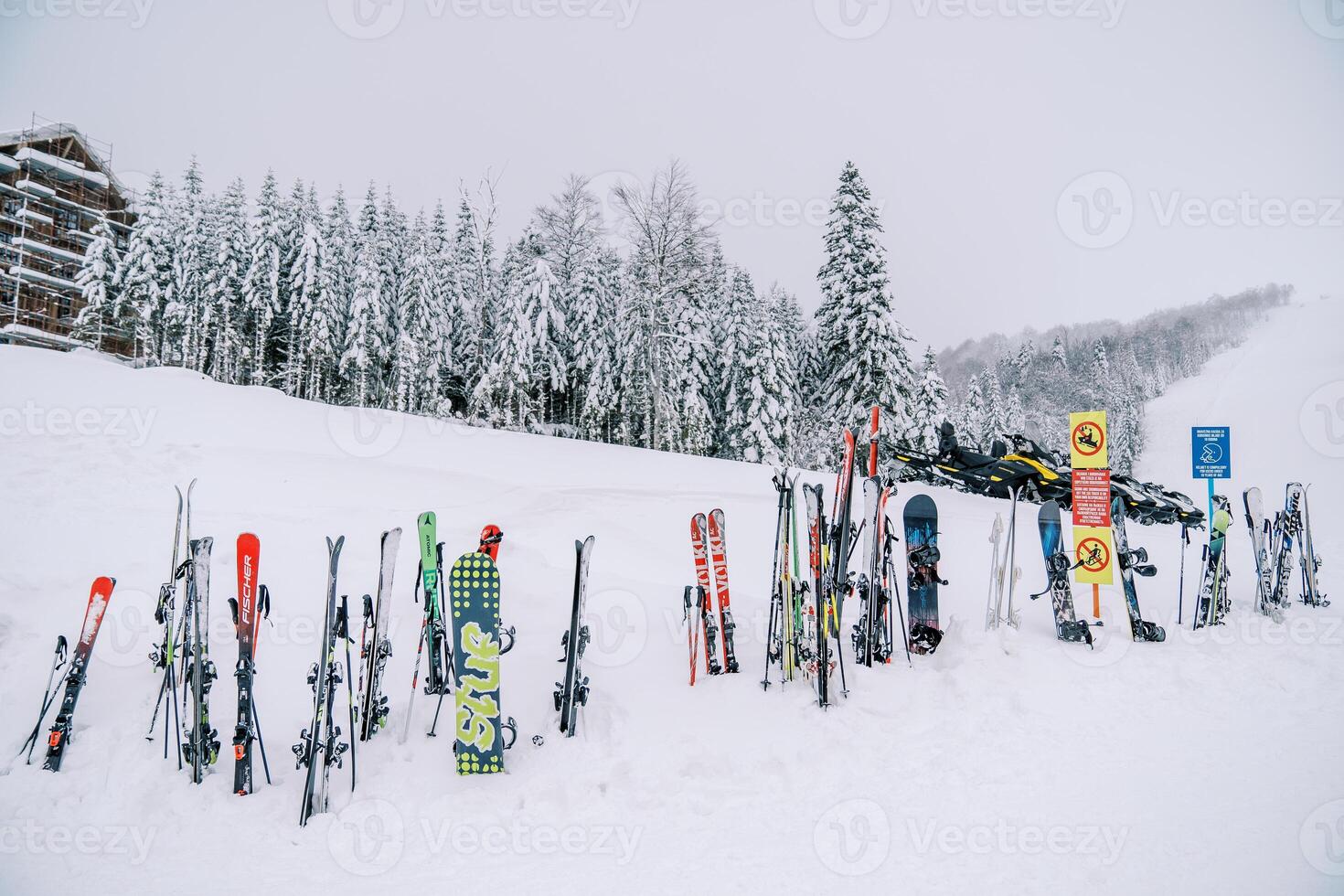 Row of colorful skis and snowboards stands stuck in the snow near a sign on the mountain at a ski resort photo