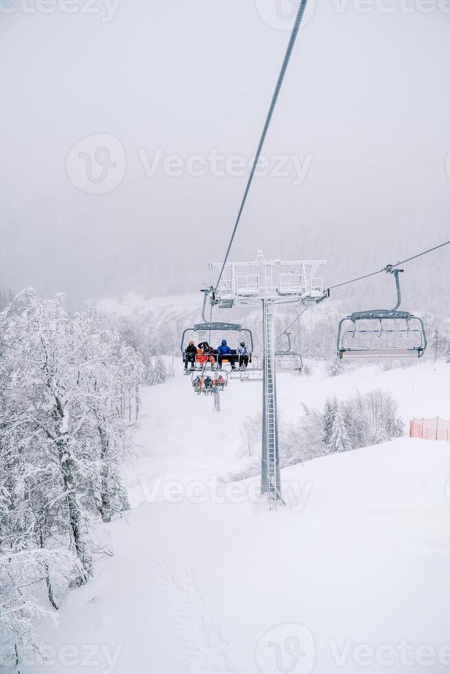 Skiers in colorful ski suits ride through the snow-capped mountains on a chairlift photo