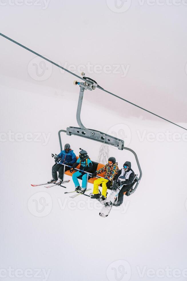 Skiers and snowboarders ride uphill through the fog on a chairlift photo