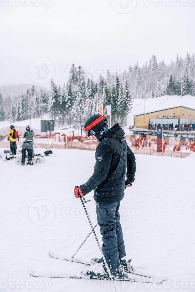 Man in a ski suit stands on skis in the snow and looks at his feet. Side view photo